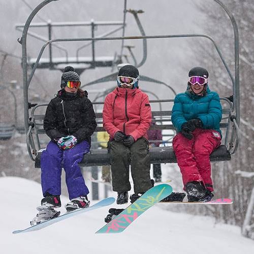 Three snowboarders on a chair at Sunday River. 